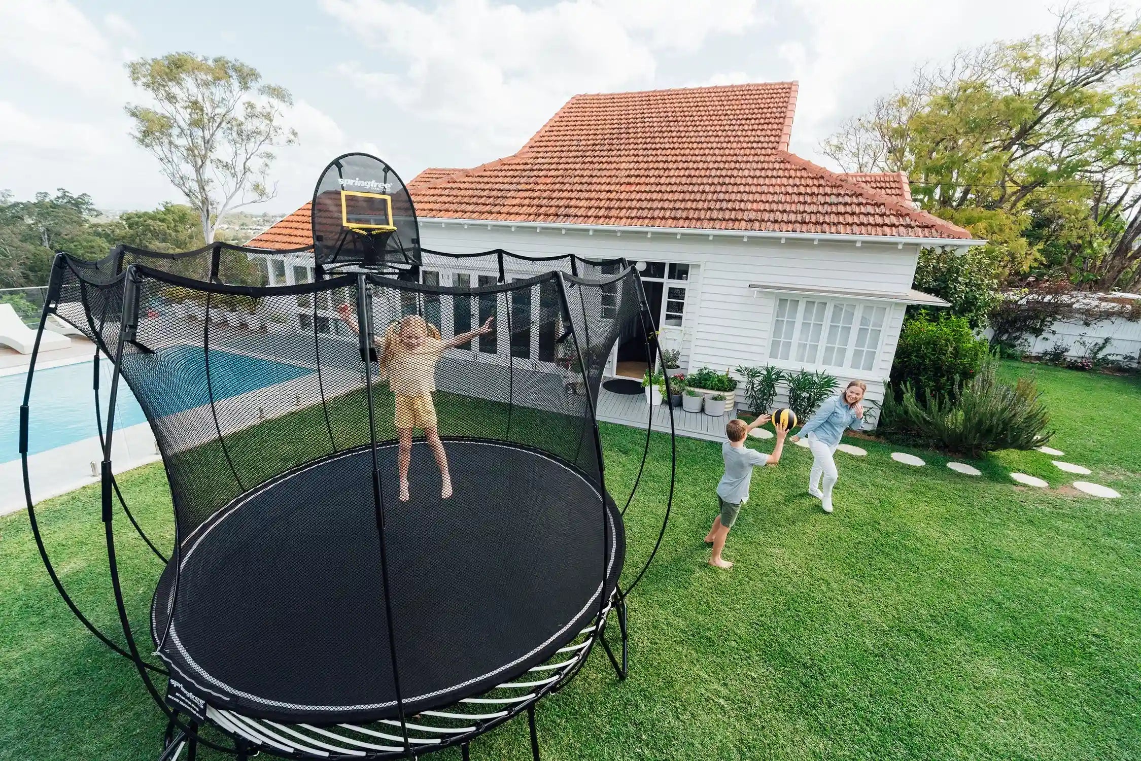 girl jumping on a trampoline while her brother and mother playing around it