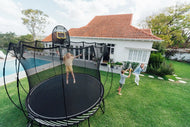 girl jumping on a trampoline while her brother and mother playing around it
